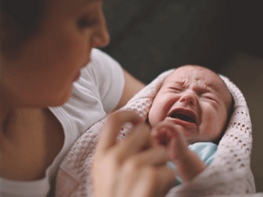 Woman holding a crying baby, trying to soothe him.