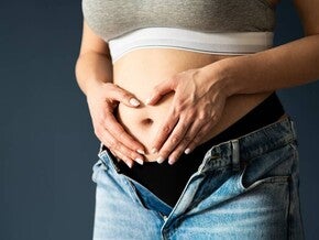 Abdomen de mujer embarazada en primer o segundo trimestre, manos en forma de corazón sobre el vientre.