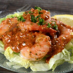 Pescado y Ensalada Criolla en un plato hay una base de ensalada y encima camarones con salsa