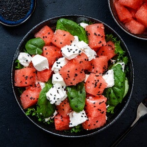 Ensalada de Sandía, Espinacas y Queso con Pan Un bowl que contiene cubos de sandía, espinacas y queso