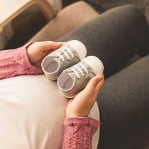 Mamá embarazada de un bebé arcoíris cogiendo unos zapatitos.