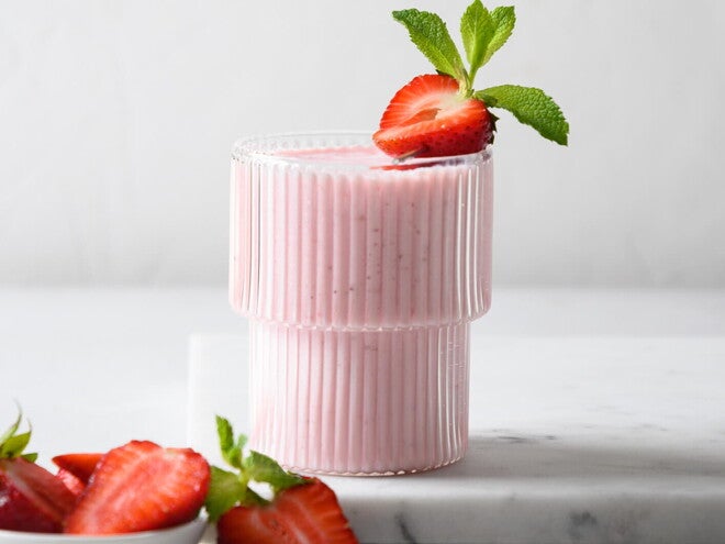 Batido Cremoso de Fresas Un vaso contiene batido de fresa y la fruta de decoración