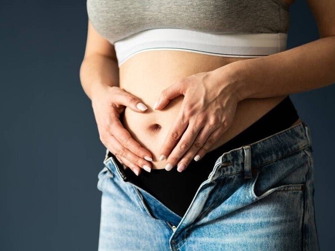 Abdomen de mujer embarazada en primer o segundo trimestre, manos en forma de corazón sobre el vientre.