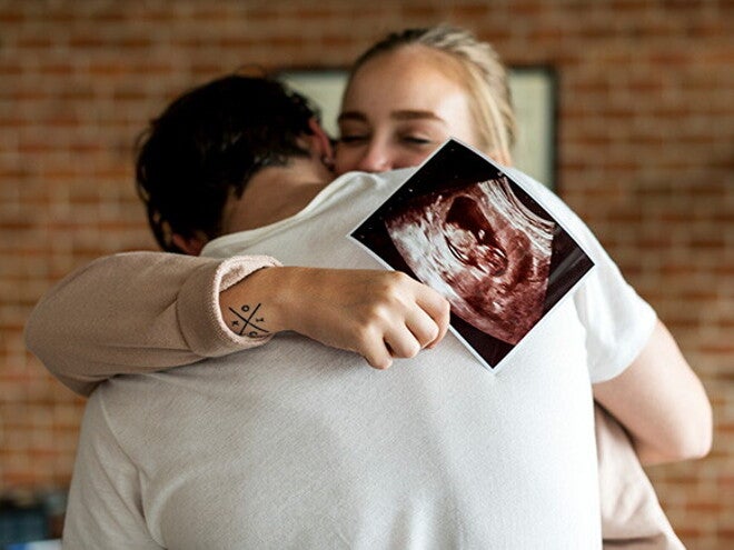 Identificar los síntomas de embarazo a tiempo es importante para prevenir riesgos Pareja abrazándose mientras la mujer sostiene una ecografía