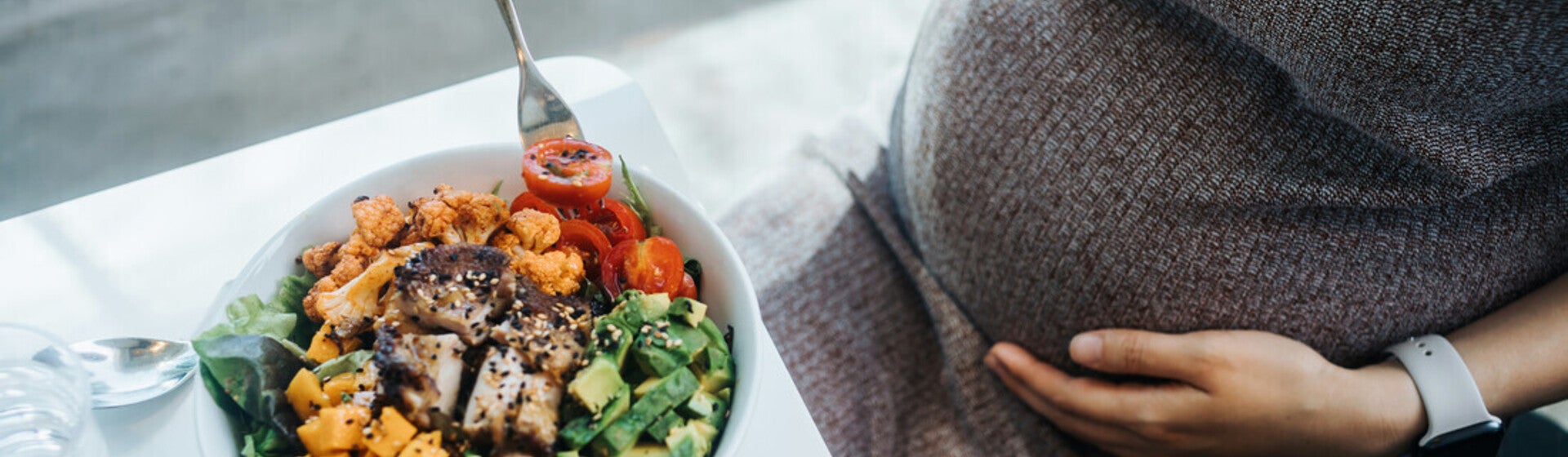 Mujer embarazada en la cocina comiendo ensalada con verduras variadas. Nutrición en el embarazo.