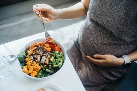 Mujer embarazada en la cocina comiendo ensalada con verduras variadas. Nutrición en el embarazo.
